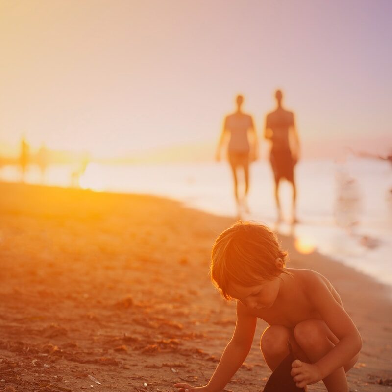 boy playing sand on seashore during sunset