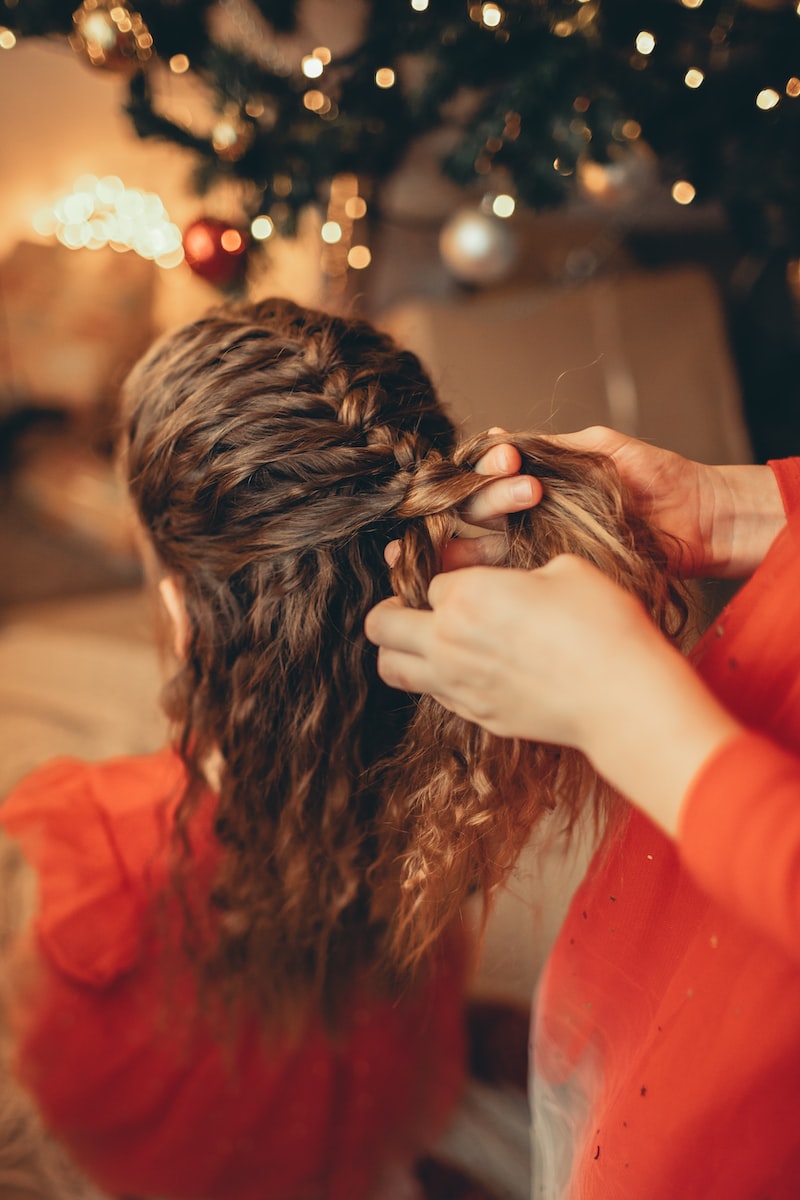 a woman is braiding her hair in front of a christmas tree